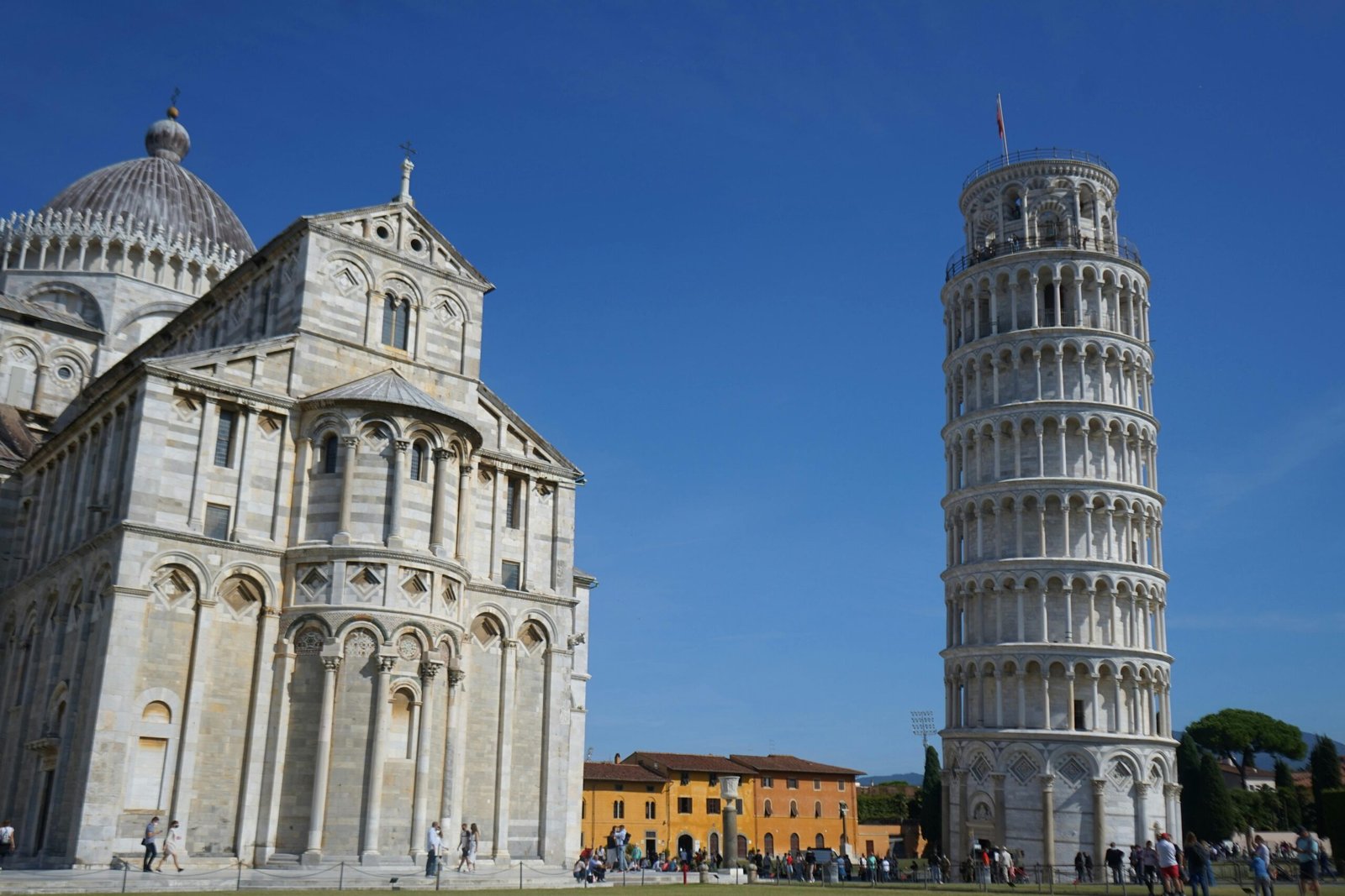 View of the Leaning Tower of Pisa and Pisa Cathedral under a clear blue sky in Tuscany, Italy.