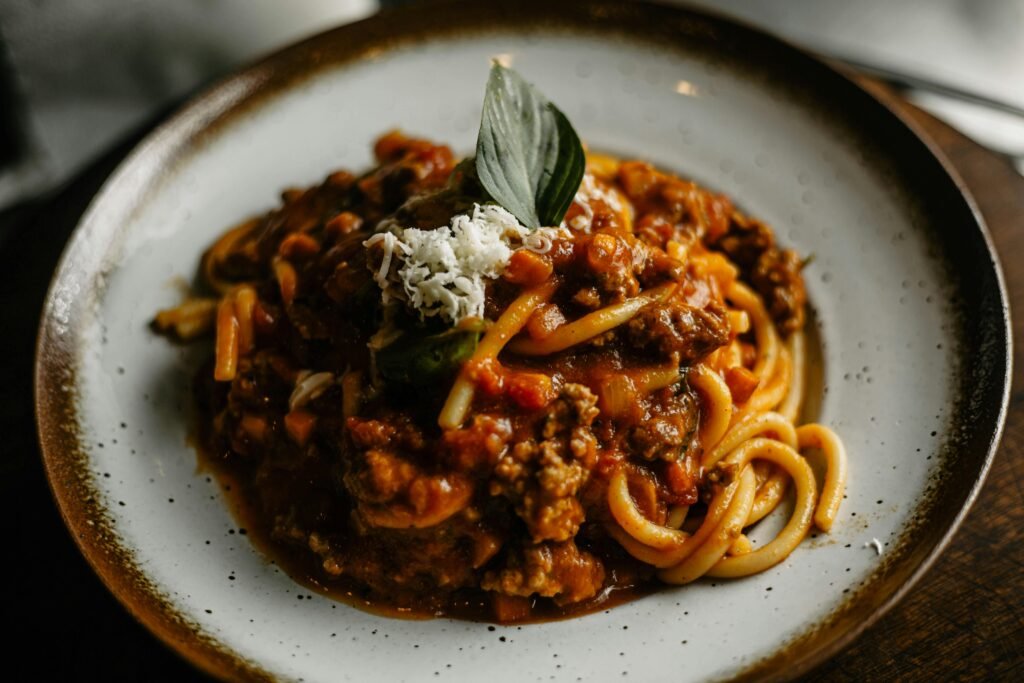 A close-up of flavorful Italian pasta with rich meat sauce garnished with basil and cheese.